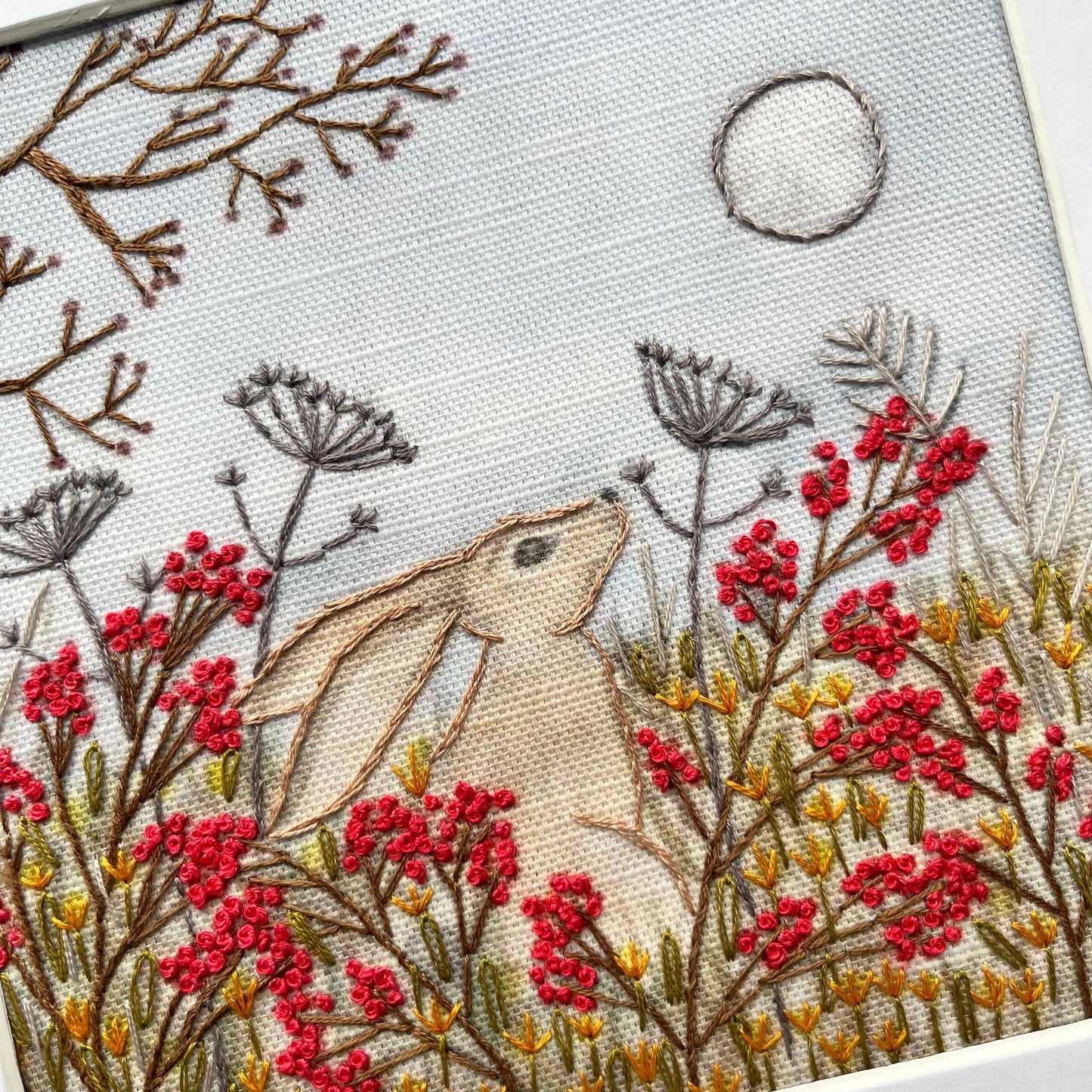 Embroidery of a hare among flowers and branches with a moon in the background