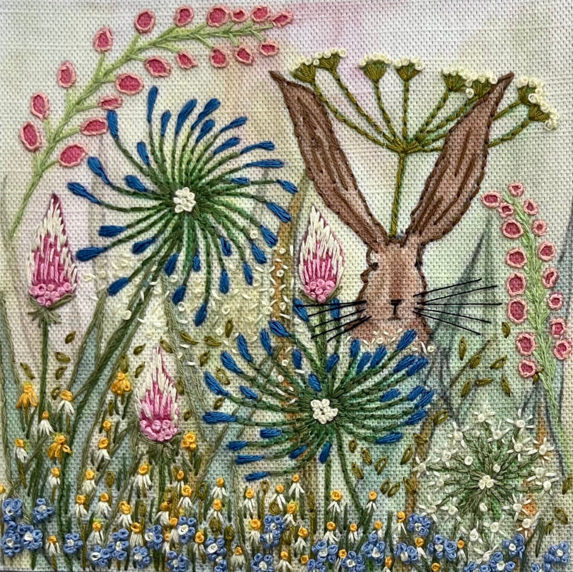 Embroidered artwork of a rabbit among flowers with a green background