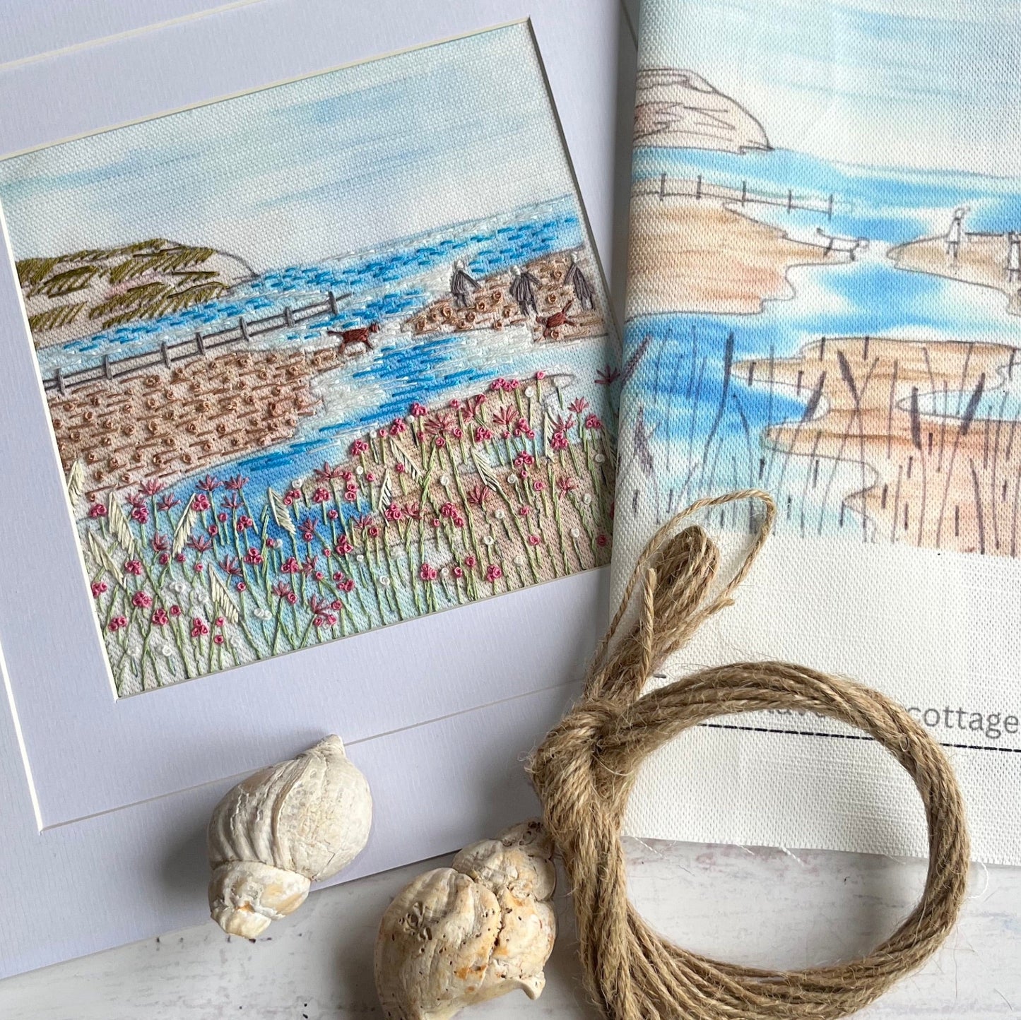Two scenic cards with a coastal landscape and seashells on a wooden surface.