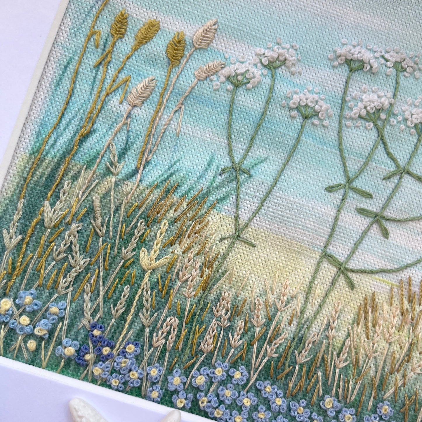 Embroidered artwork of a natural scene with plants and flowers, featuring a starfish and shell on a white background.