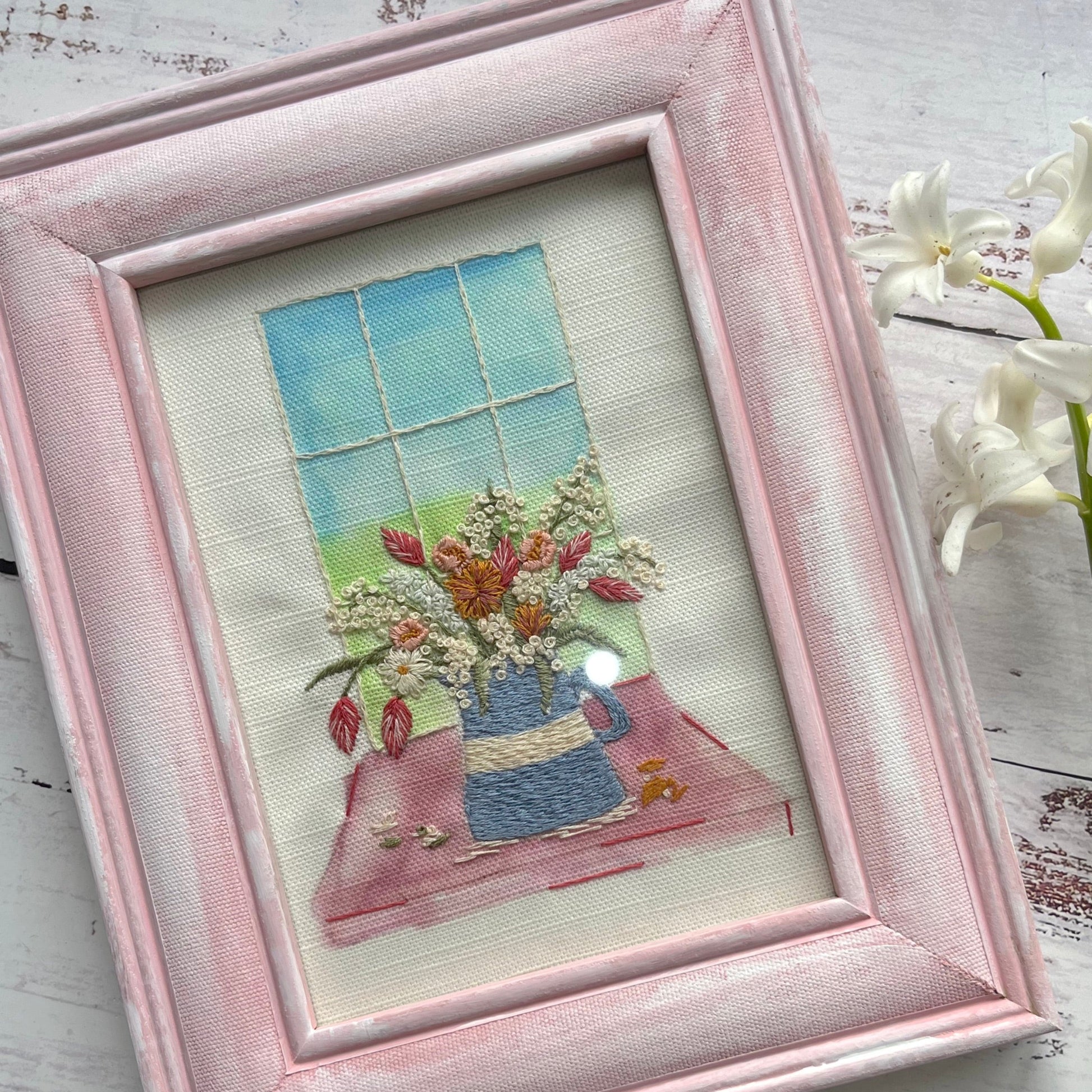 Framed embroidered picture of a window with flowers on a textured surface
