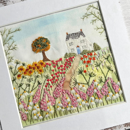 Embroidered scene of a house with flowers and trees on a white background