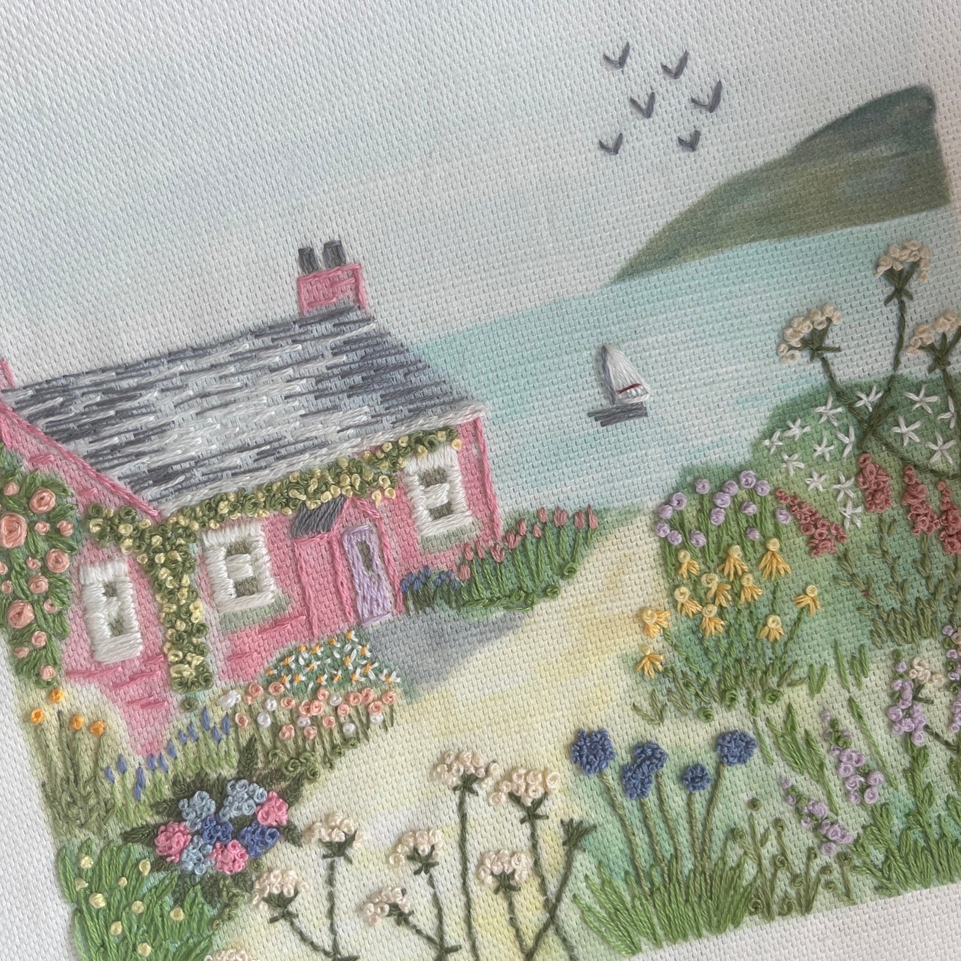 Embroidered scene of a house with a garden and sailboat on water