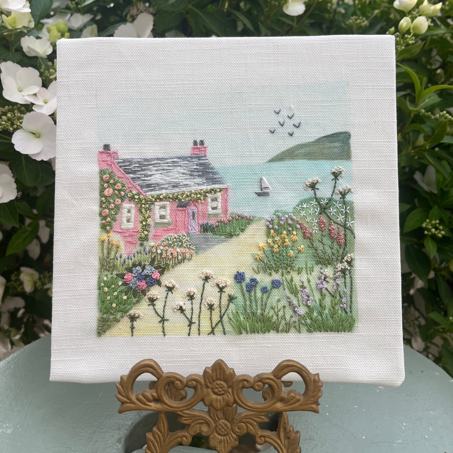 Embroidered scene of a pink house with a garden on a white fabric background