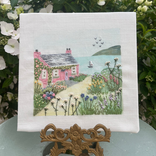 Embroidered scene of a pink house with a garden on a white fabric background