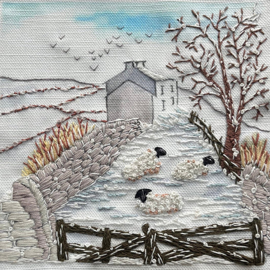 Embroidered scene of a snowy landscape with a house, trees, and sheep.