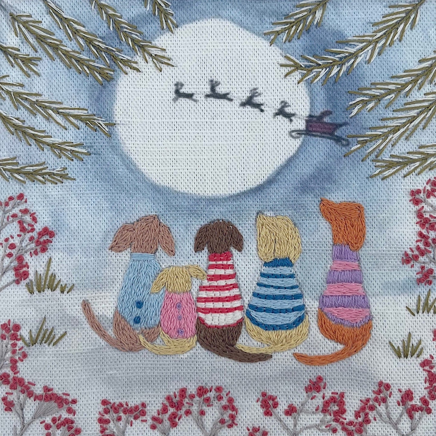 Embroidered scene of dogs in colorful sweaters looking at a full moon with reindeer sleigh.