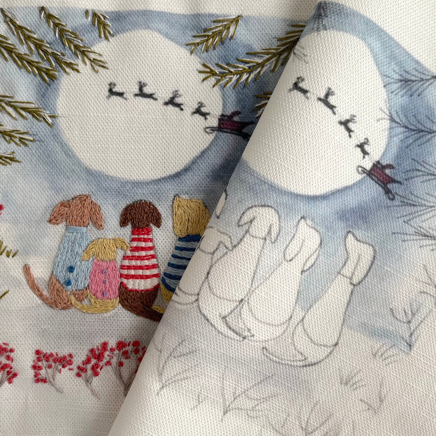 Embroidered fabric with winter-themed design featuring a moon, trees, and animals.
