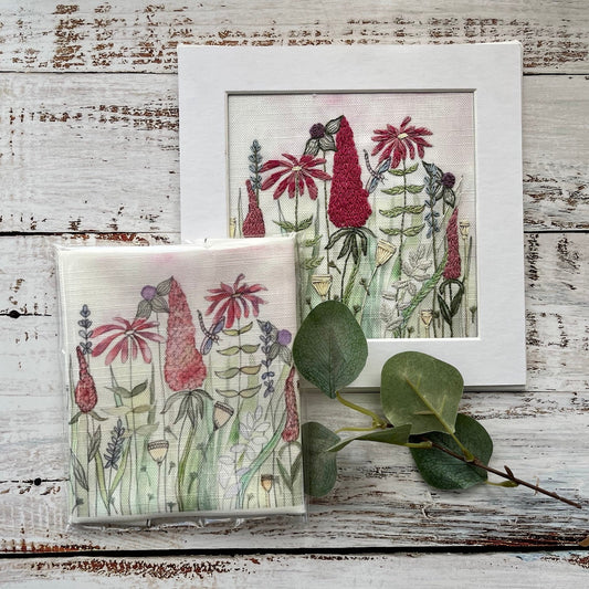 Two framed artworks of floral and bird designs on a rustic wooden surface.