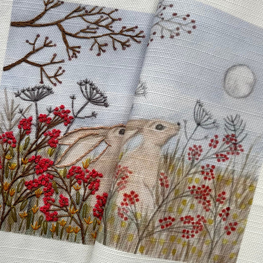 Two embroidered fabric swatches with floral and moon designs on a textured surface.