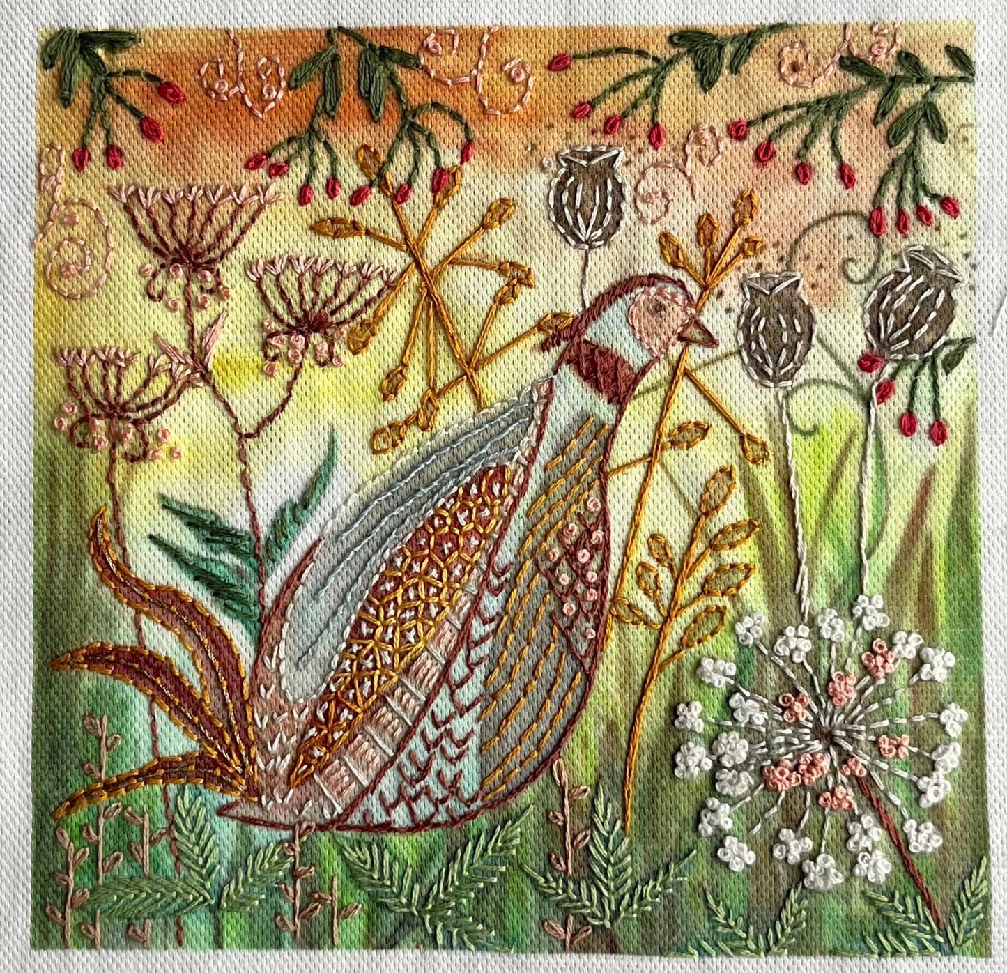 Embroidered design of a bird among flowers and plants on fabric.