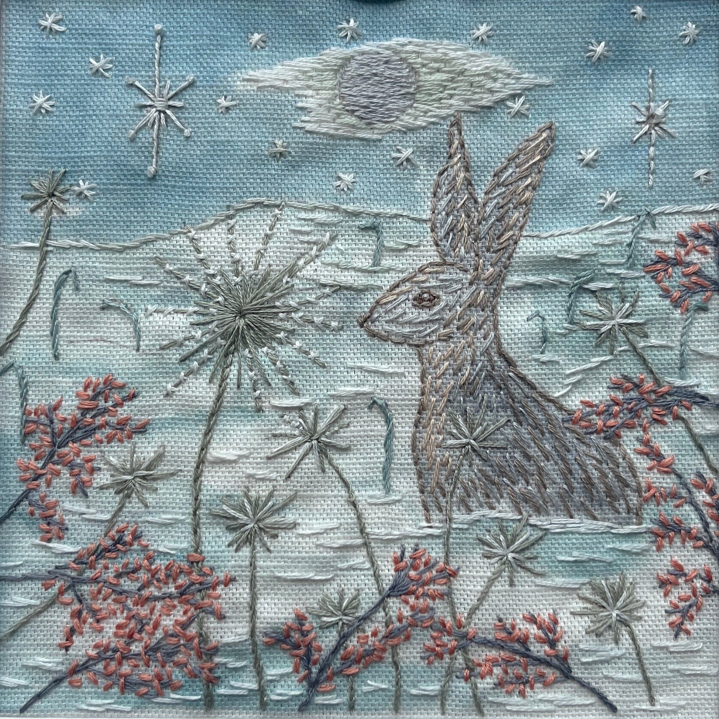 Embroidered artwork of a hare among flowers and stars on a blue background