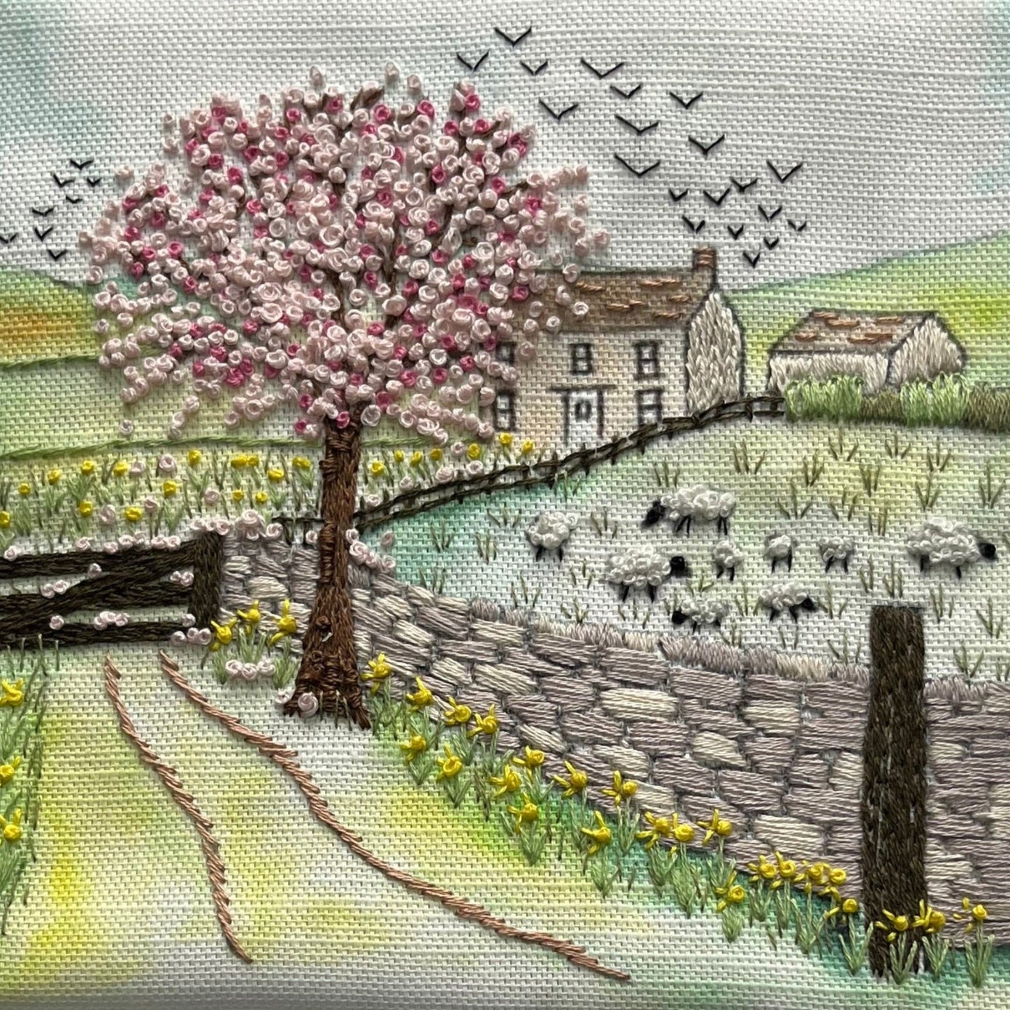 Embroidery of a pastoral scene with a cherry blossom tree, house, and animals.