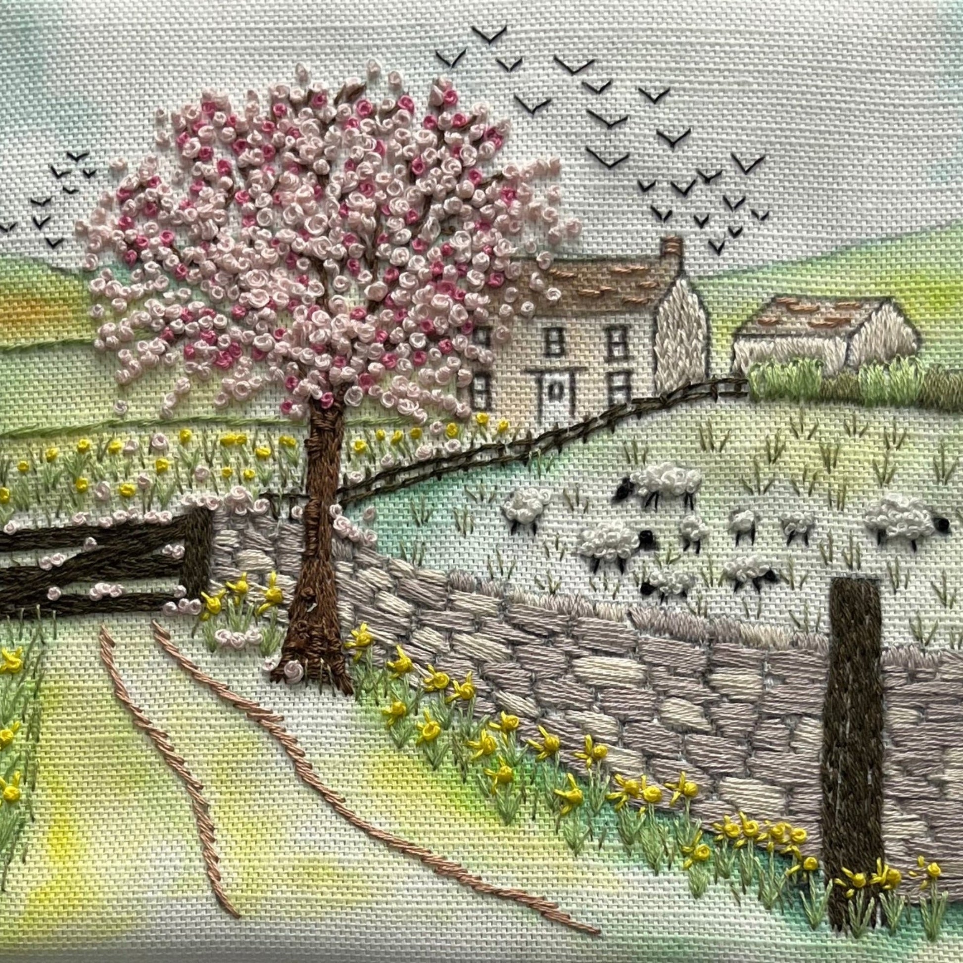 Embroidery of a pastoral scene with a cherry blossom tree, house, and animals.