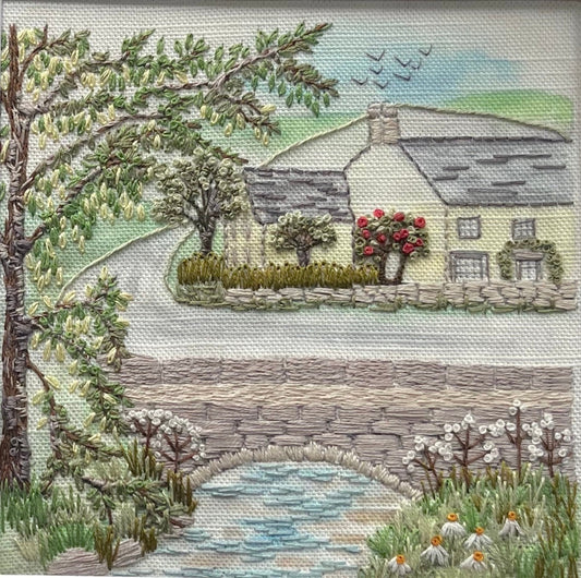 Embroidered scene of a house, trees, and a bridge with a stone wall.