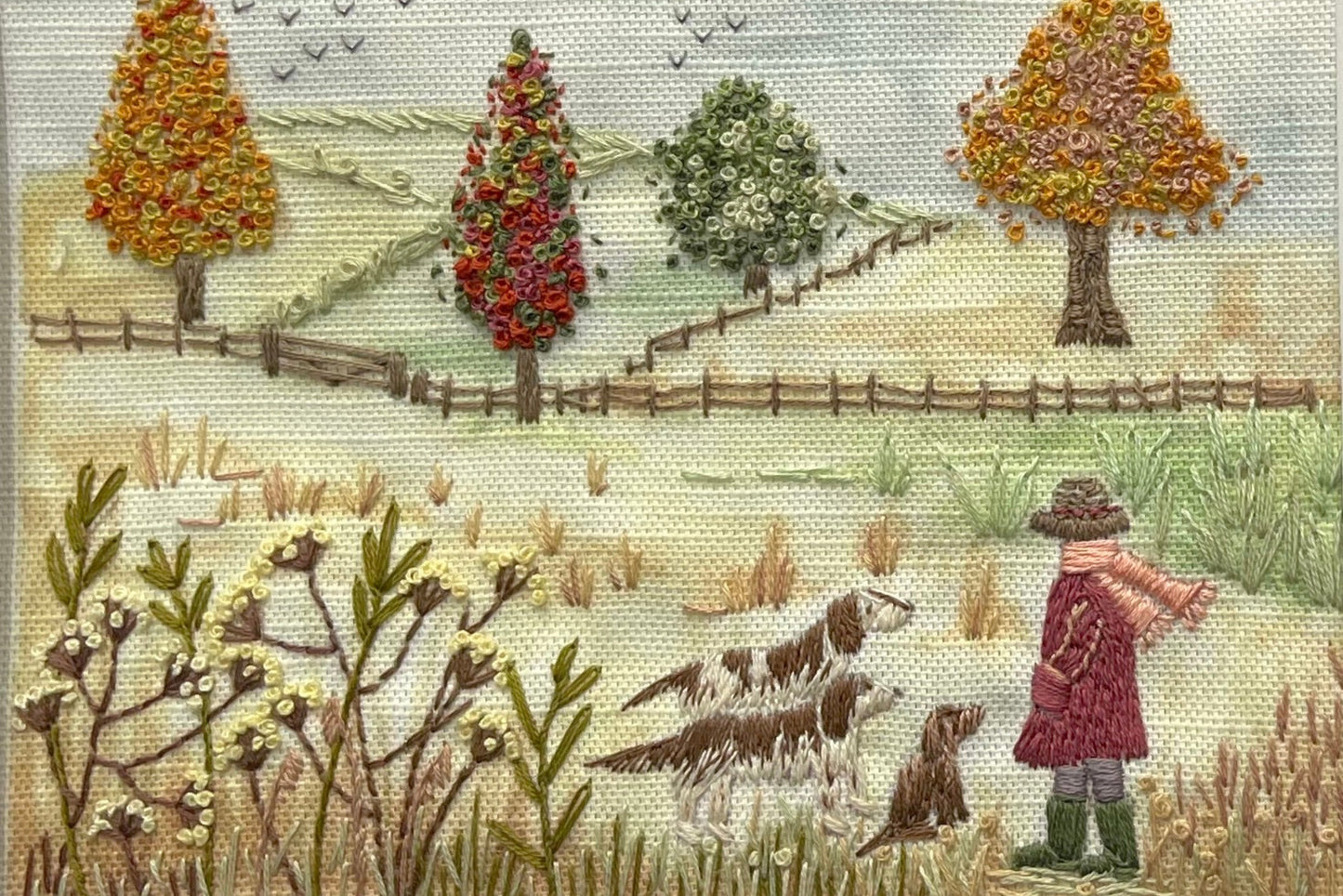 Embroidered scene with a person, two dogs, and trees in a field.