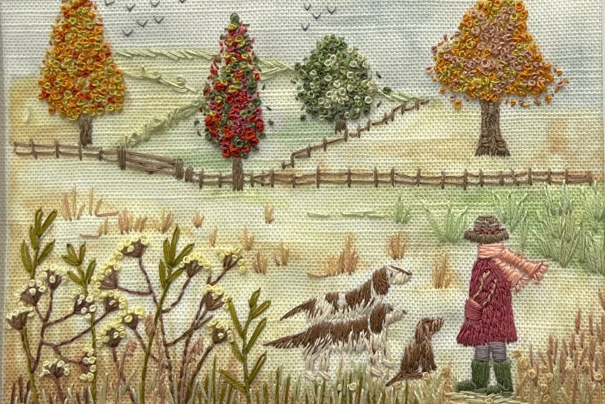 Embroidered scene with a person, two dogs, and trees in a field.