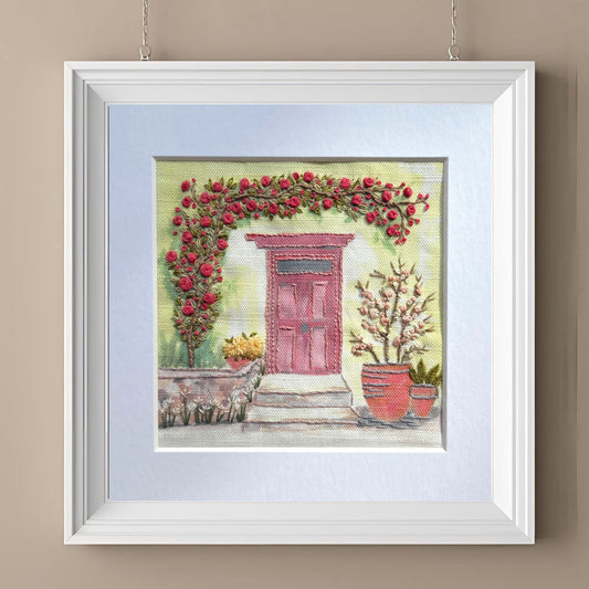 Framed artwork of a pink door with floral arch on a beige wall
