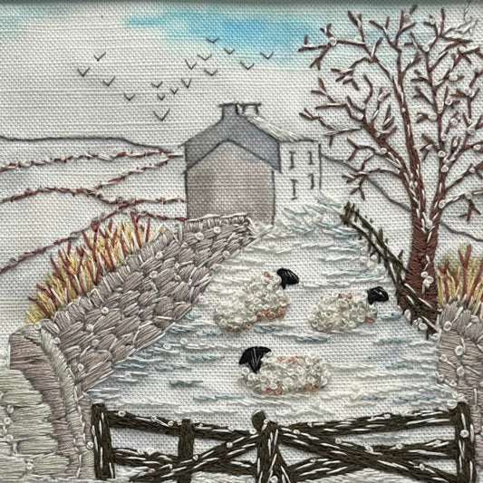 Embroidered scene of sheep in a snowy landscape with a house and trees.