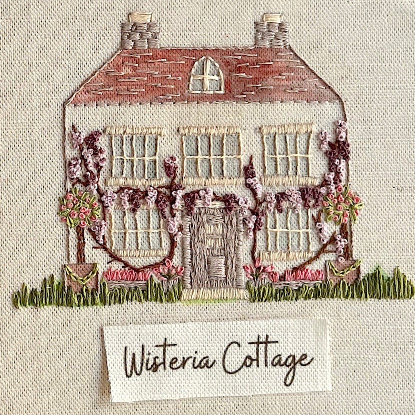 Embroidered design of a house with wisteria vines on a textured fabric background.