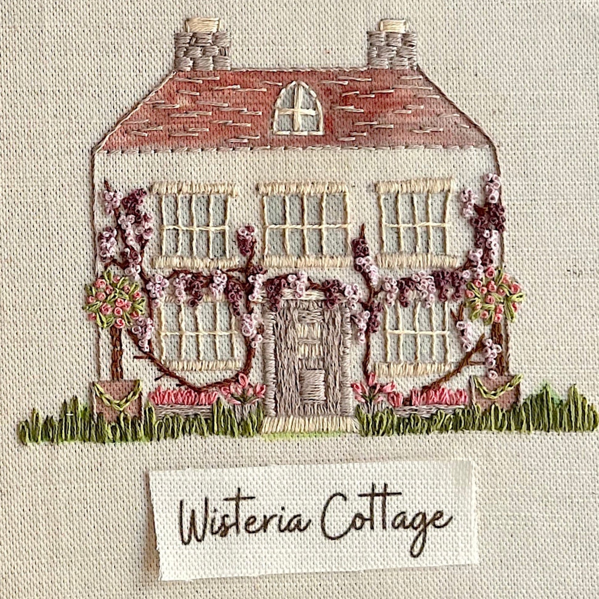 Embroidered design of a house with wisteria vines on a textured fabric background.