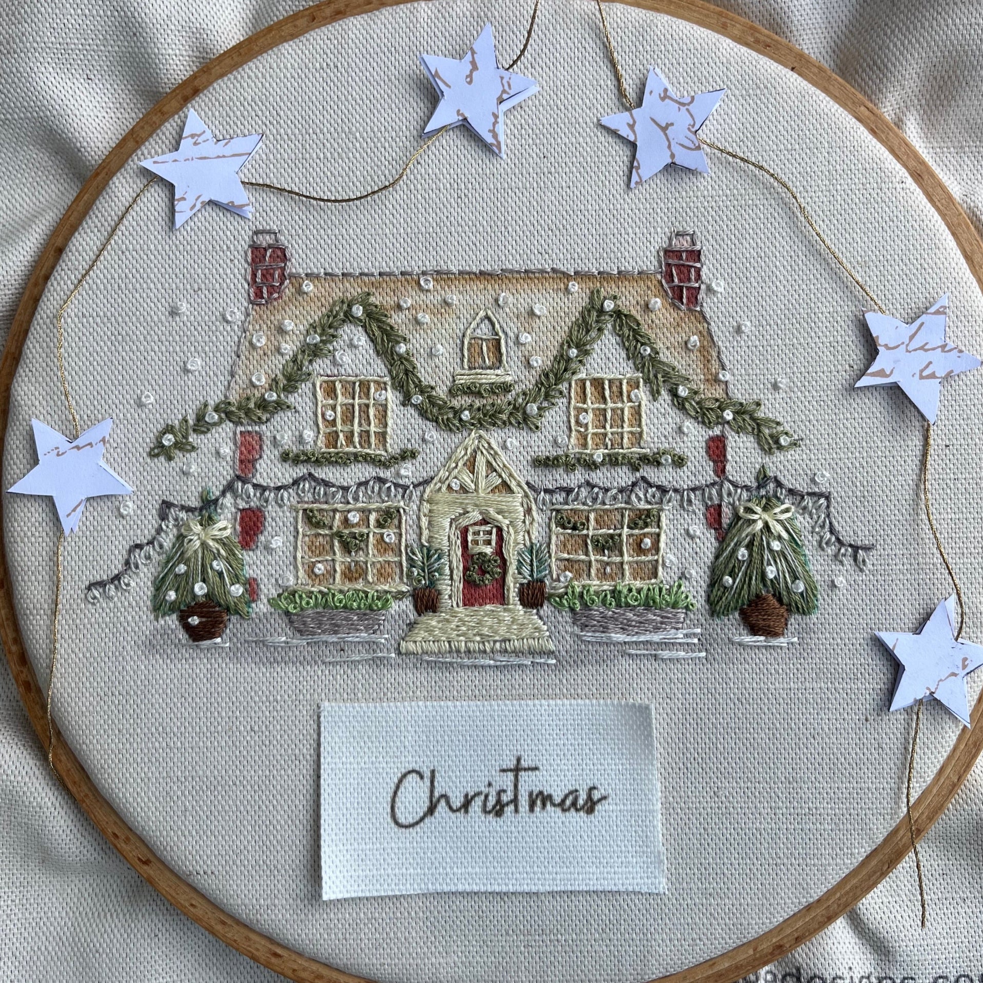 Embroidery hoop with a Christmas-themed house design and decorative stars.